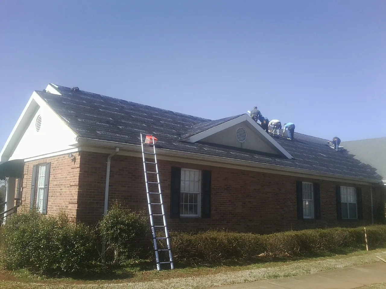 Crew tearing shingles off a brick ranch roof with a ladder set — Metal Roof Repair work by our crew in Weaverville