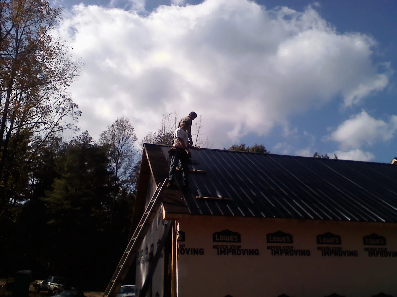 Roofer fastening dark metal panels high against a cloudy sky, from a Roof Inspection job in Weaverville